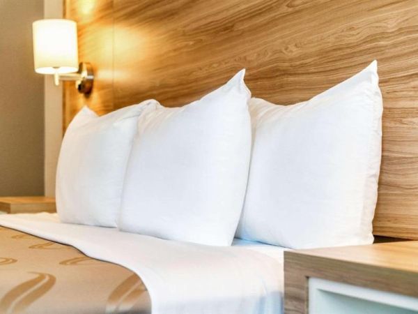 A neatly made hotel bed with white pillows and a soft-lit headboard, inviting and tidy.