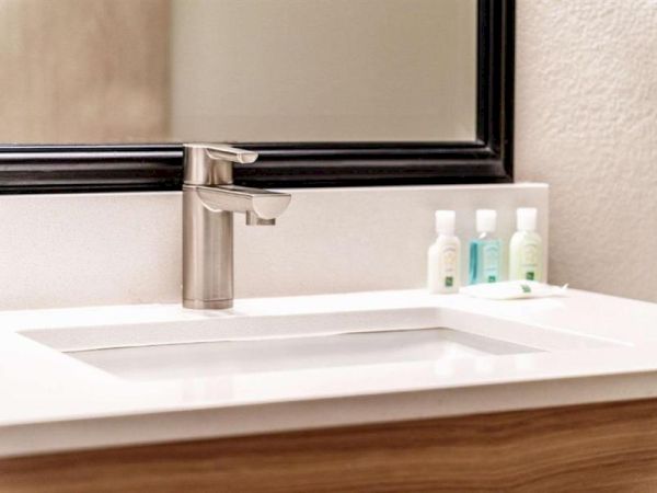 A modern bathroom sink with a sleek faucet, wide mirror, and small bottles of toiletries on the counter, all on a white countertop.