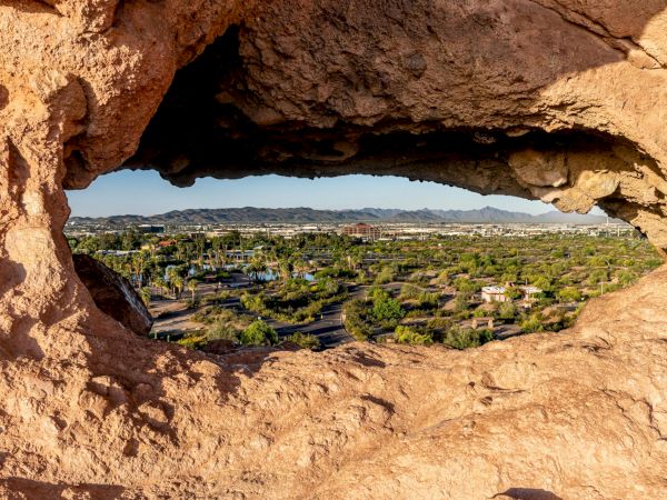A rocky desert canyon frame looks out onto a green valley and town in the distance, with clear blue sky and distant hills.